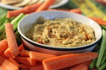 A bowl of hummus surrounded by carrots and celery